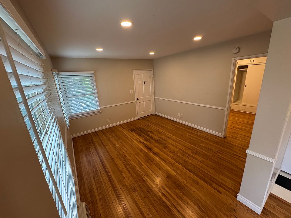 Photo taken from dining room looking into living room toward front door with bedroom visible through the open door on the right.