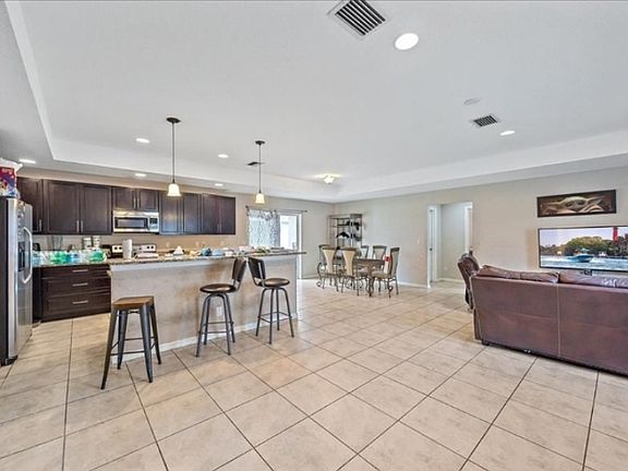 Bright and spacious open-concept living area featuring a large tile floor, modern kitchen with breakfast bar seating, and a separate dining space, perfect for entertaining or family gatherings.