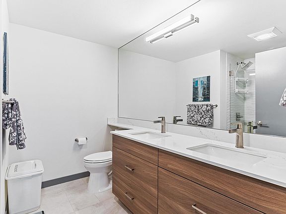 Generous primary bath with custom tile work, glass shower doors, double vanity, quartz countertops, and plenty of storage