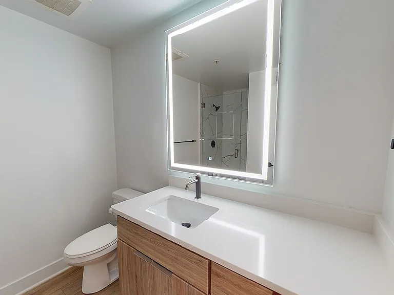 Apartment bathroom with wood-style flooring and an LED vanity mirror.