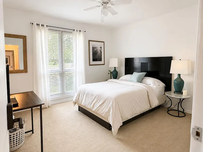 Well-appointed bedroom with a full bed, large window with blinds and curtains, ceiling fan, and convenient bedside tables.